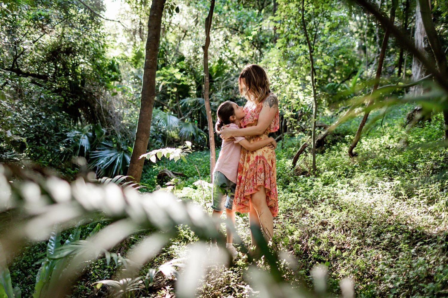 Two people sharing an embrace in a sunlit forest clearing.