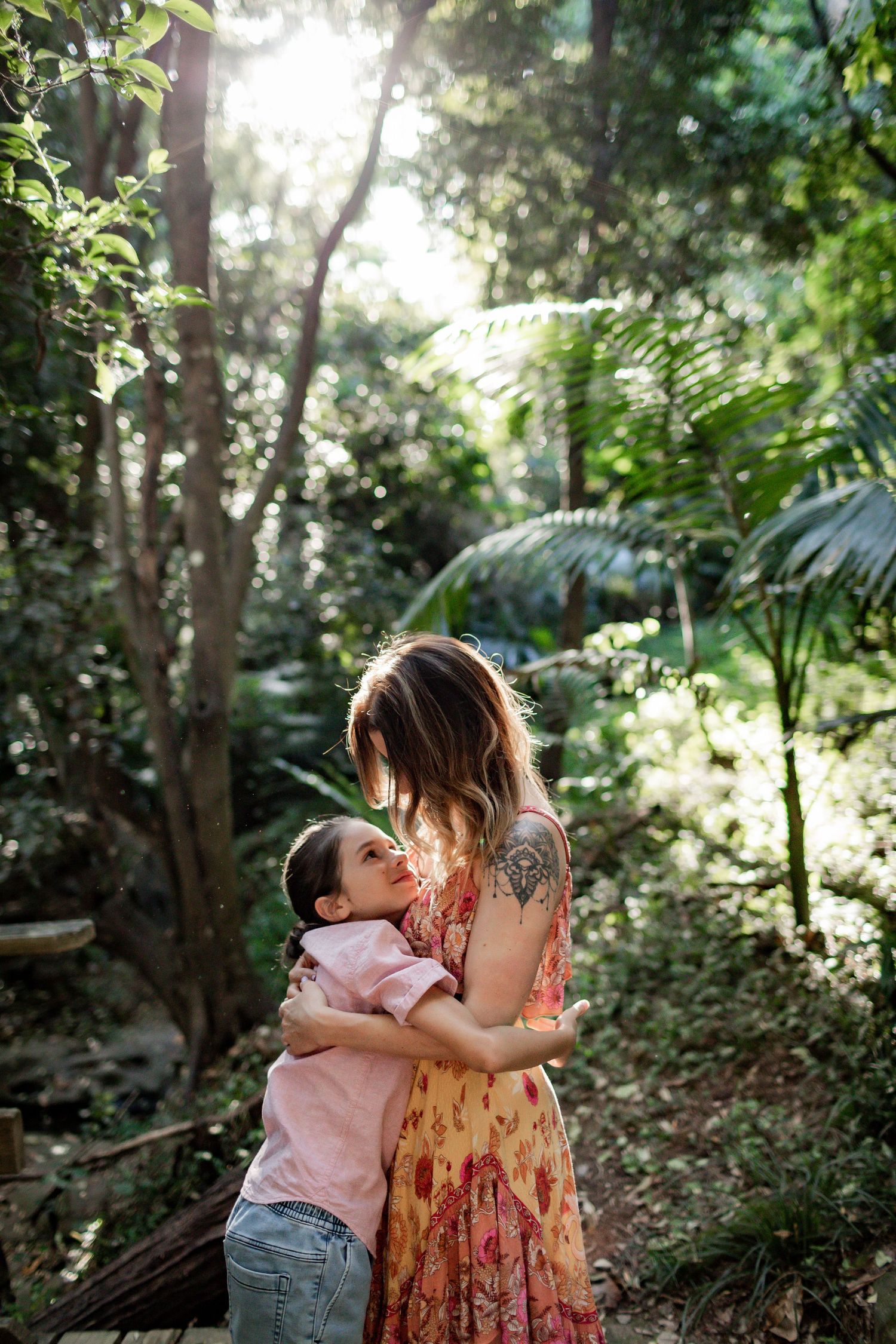 A tender embrace captured in a sunlit forest with palm fronds and trees in the background.