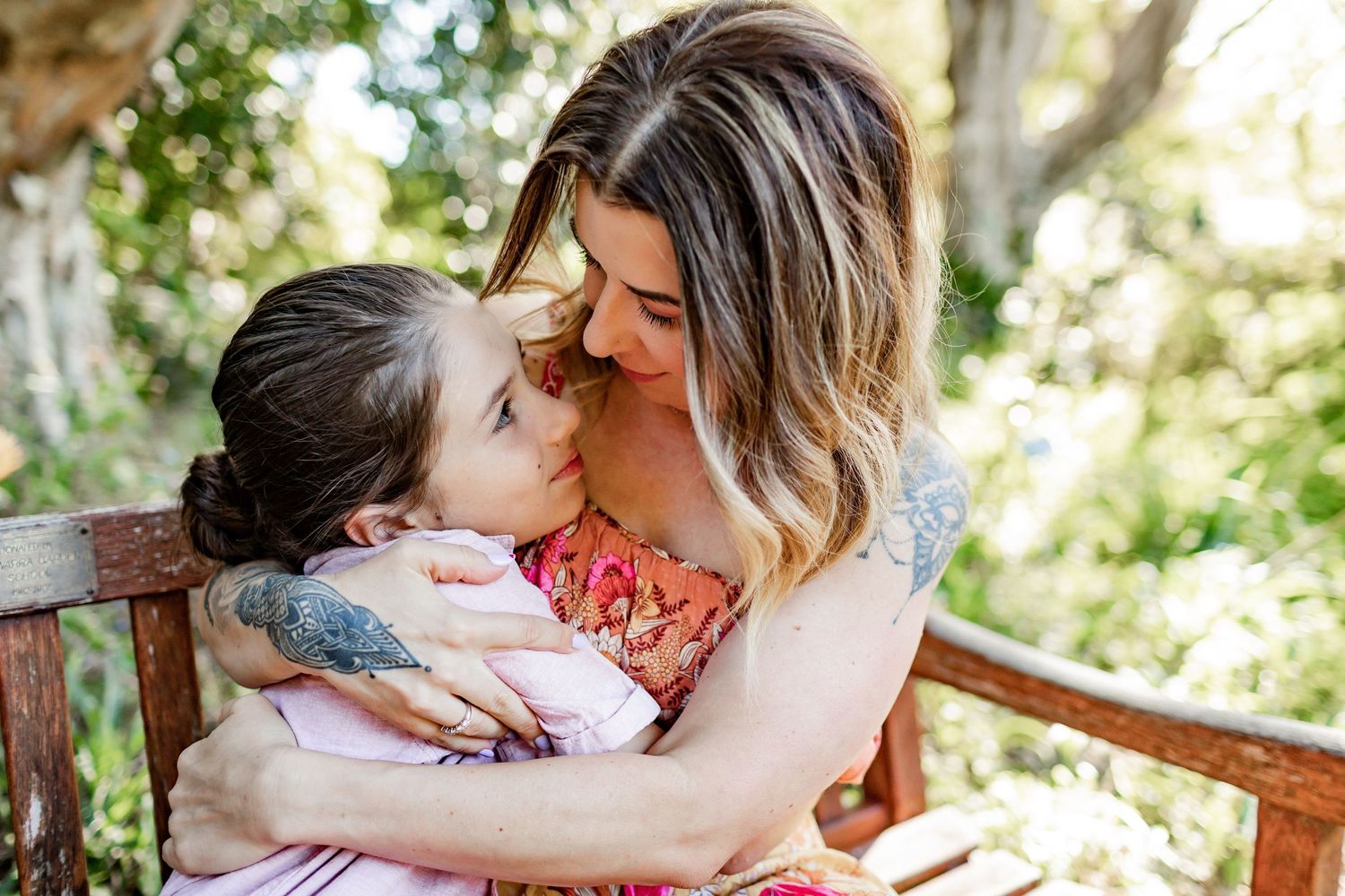 An intimate embrace shared on a wooden bench in a sunny garden setting.