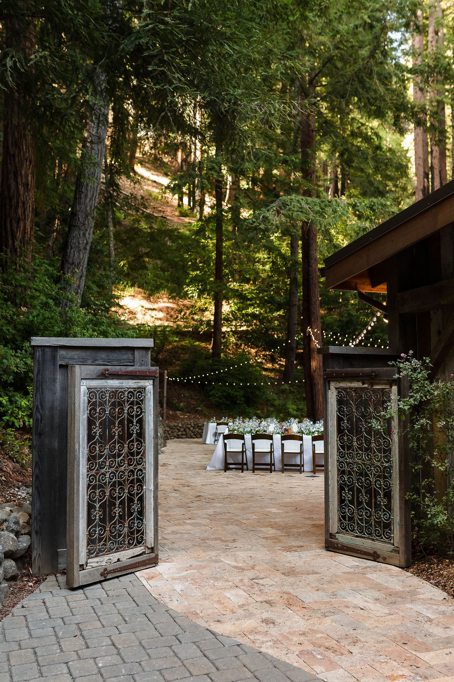 Ornate wooden doors open to reveal a wedding reception setup along a forest path.