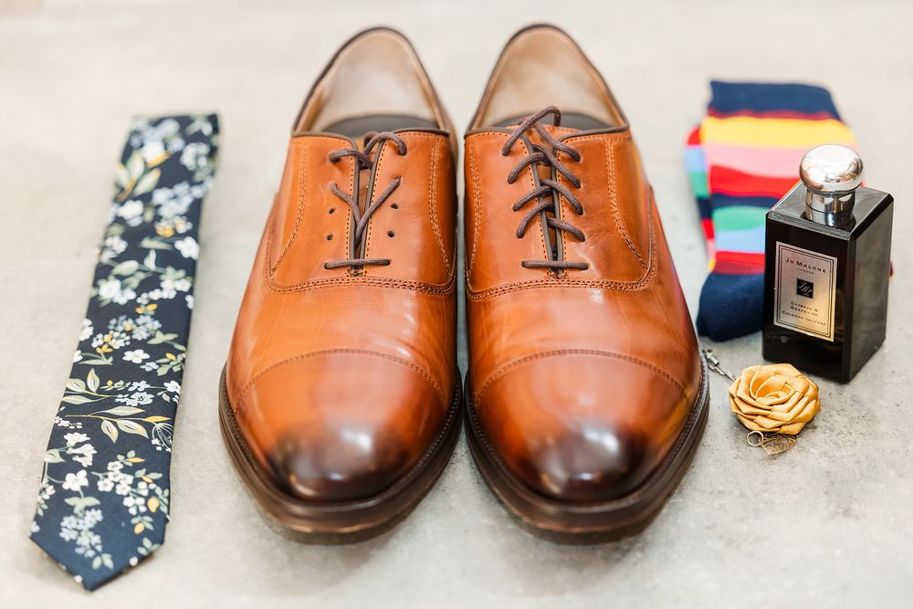 Brown leather dress shoes with floral tie and perfume bottle arranged as wedding accessories.