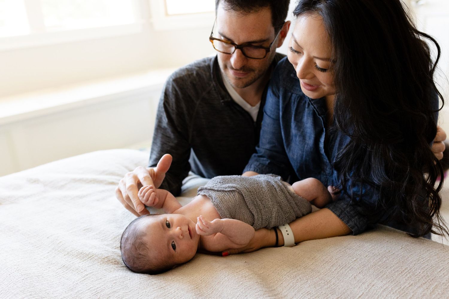 Mother and Father gaze down at their daughter during their newborn photography session in Lafayette, Colorado