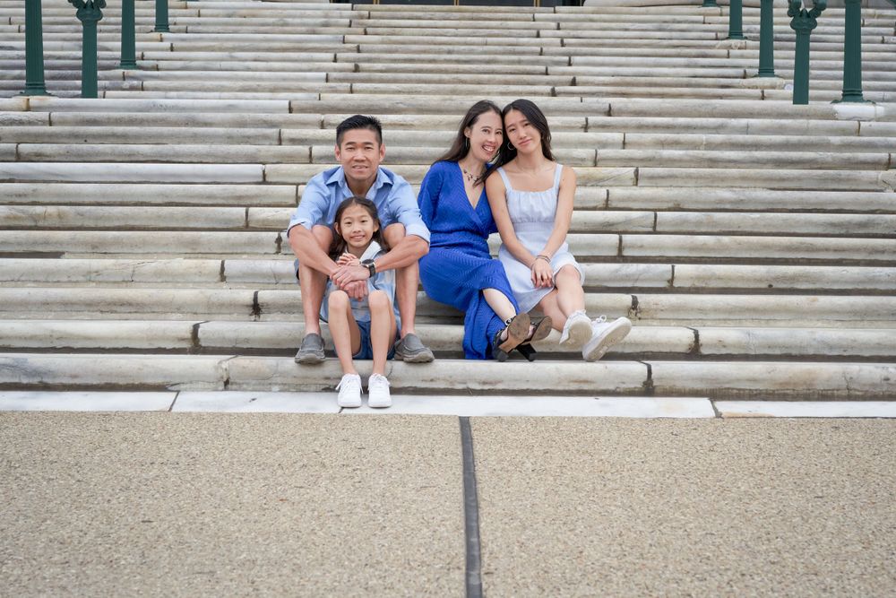 A family sits together on wide stone steps wearing coordinated blue and white outfits on a sunny day.
