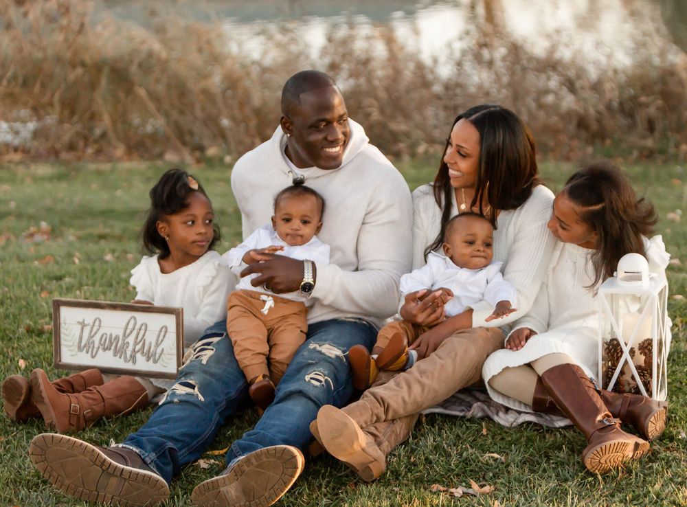 A family sits together outdoors for a casual portrait session with a 'Thankful' sign.