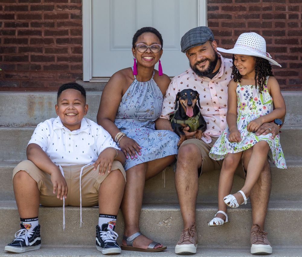 A family and their dachshund sit together on front porch steps of a brick house.