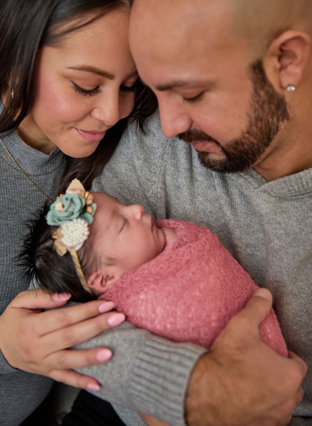 A tender moment with a newborn baby wearing a pink wrap and floral headband.