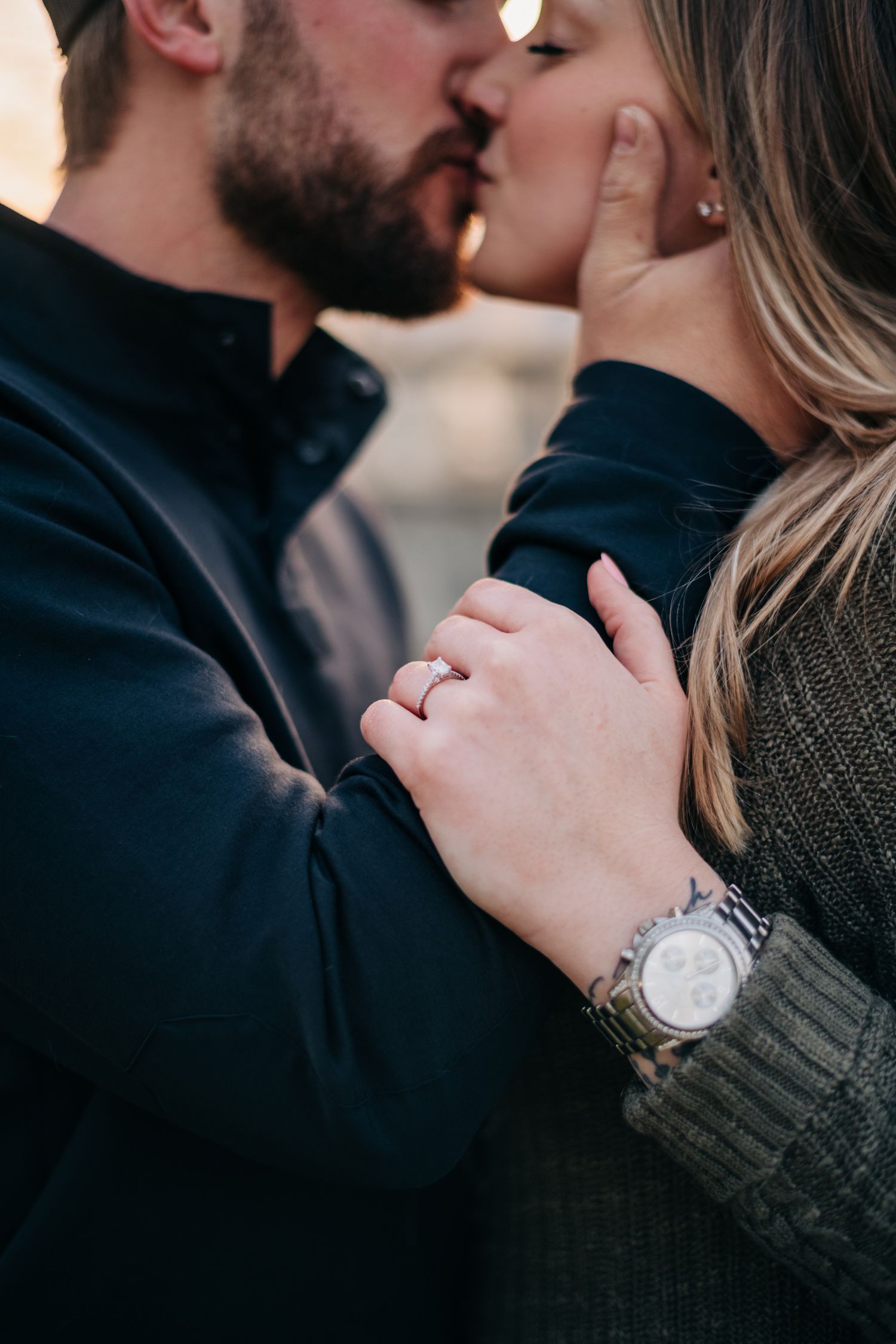 engaged couple kissing with engagement ring in focus in the foreground