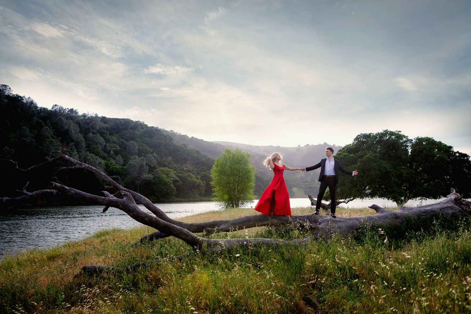 Engagement photoshoot by the lake and mountain woman in red long dress dancing with her fiancé smiling at each other