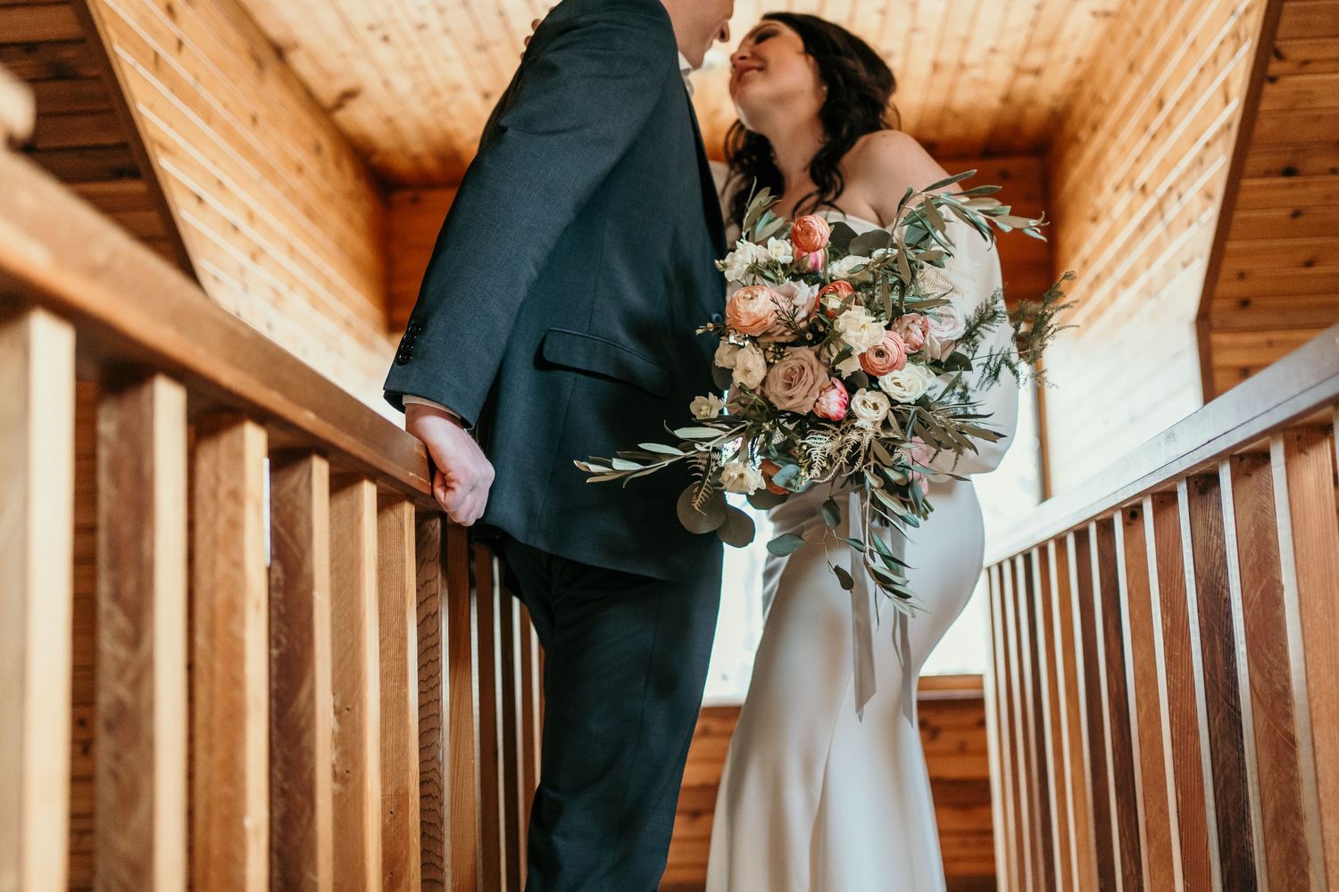 Wedding couple embracing on wooden stairs with bride holding floral bouquet.