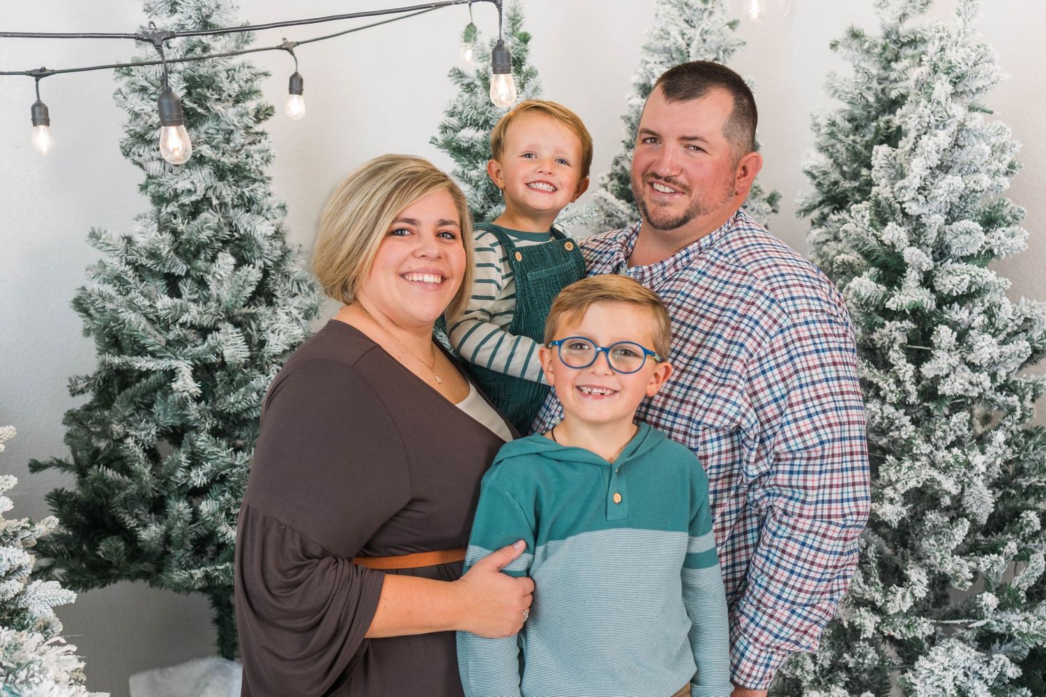 A festive family portrait with snow-flocked Christmas trees in the background.