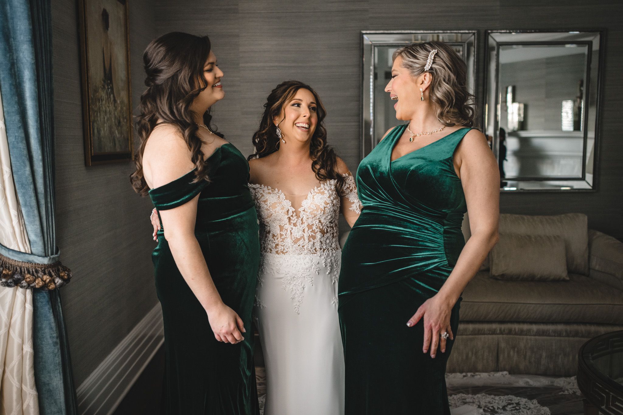 Wedding party helping with final dress adjustments in a dimly lit room.
