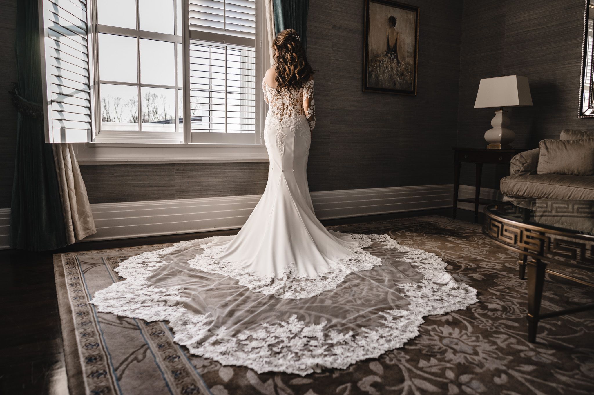 Wedding dress with long train and lace details photographed against natural window light.