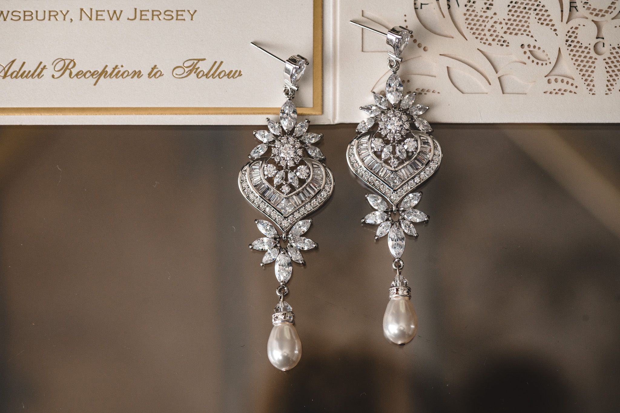 Ornate crystal and pearl drop earrings photographed against wedding invitation.