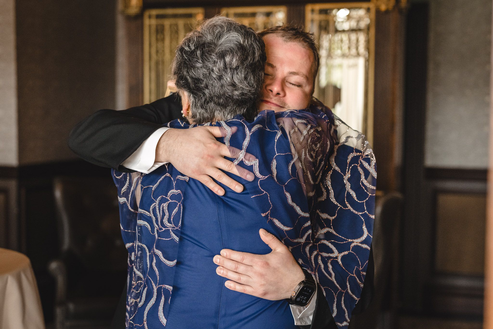 Emotional embrace captured in blue formal attire during wedding celebration.