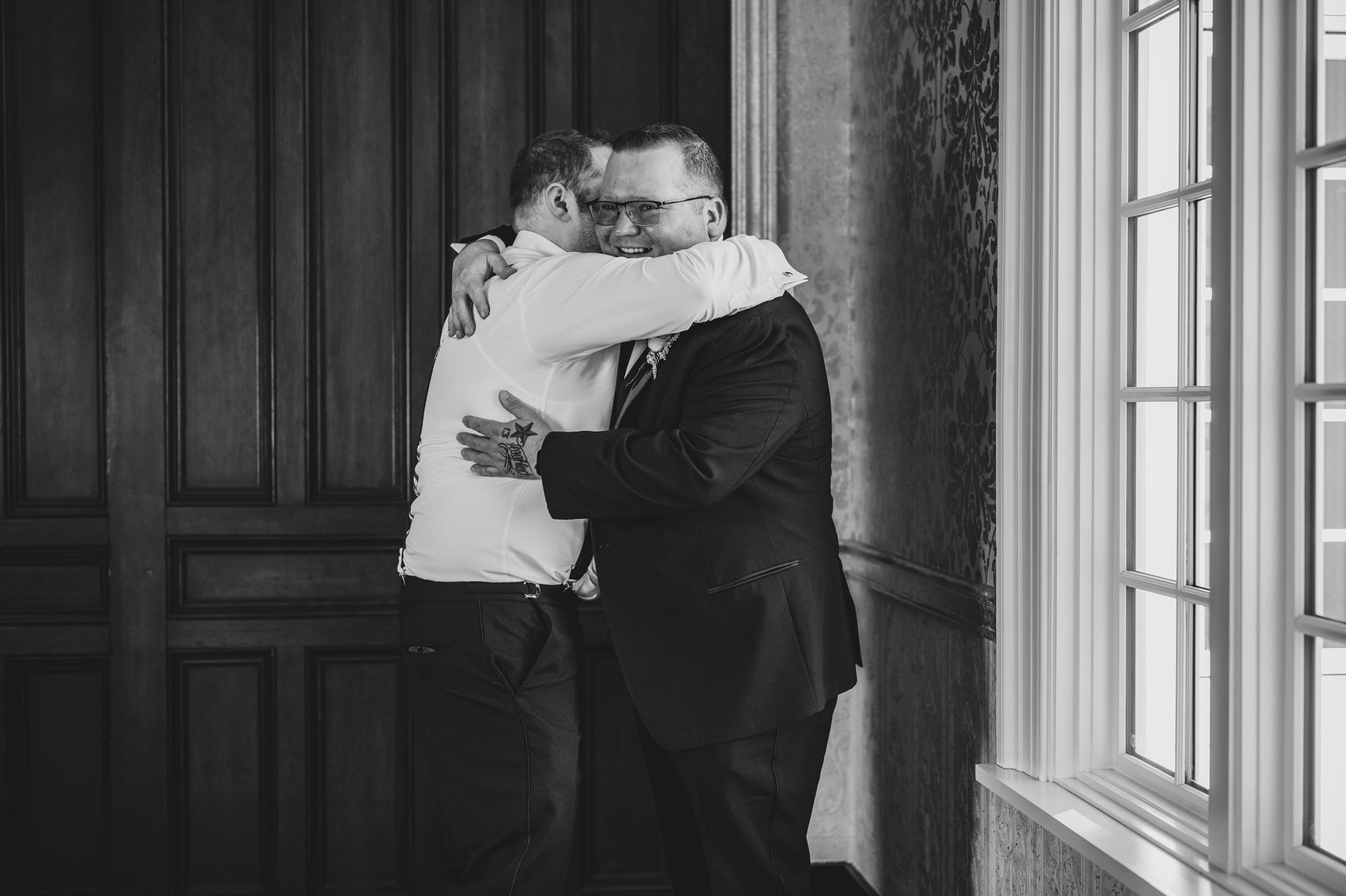 Two people in formal wear embrace in an emotional black and white moment.