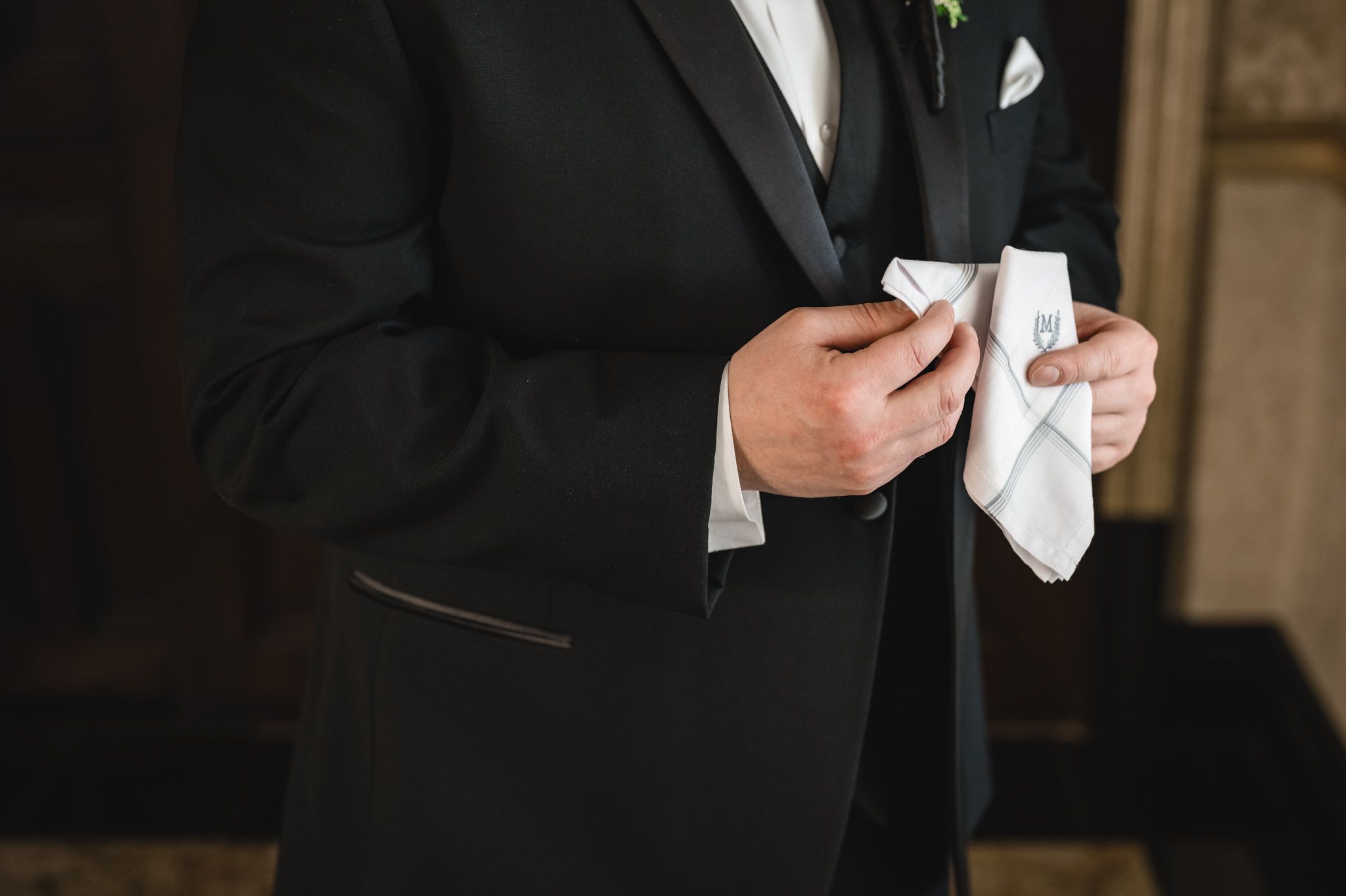 Close-up of hands holding a white handkerchief against a black tuxedo.