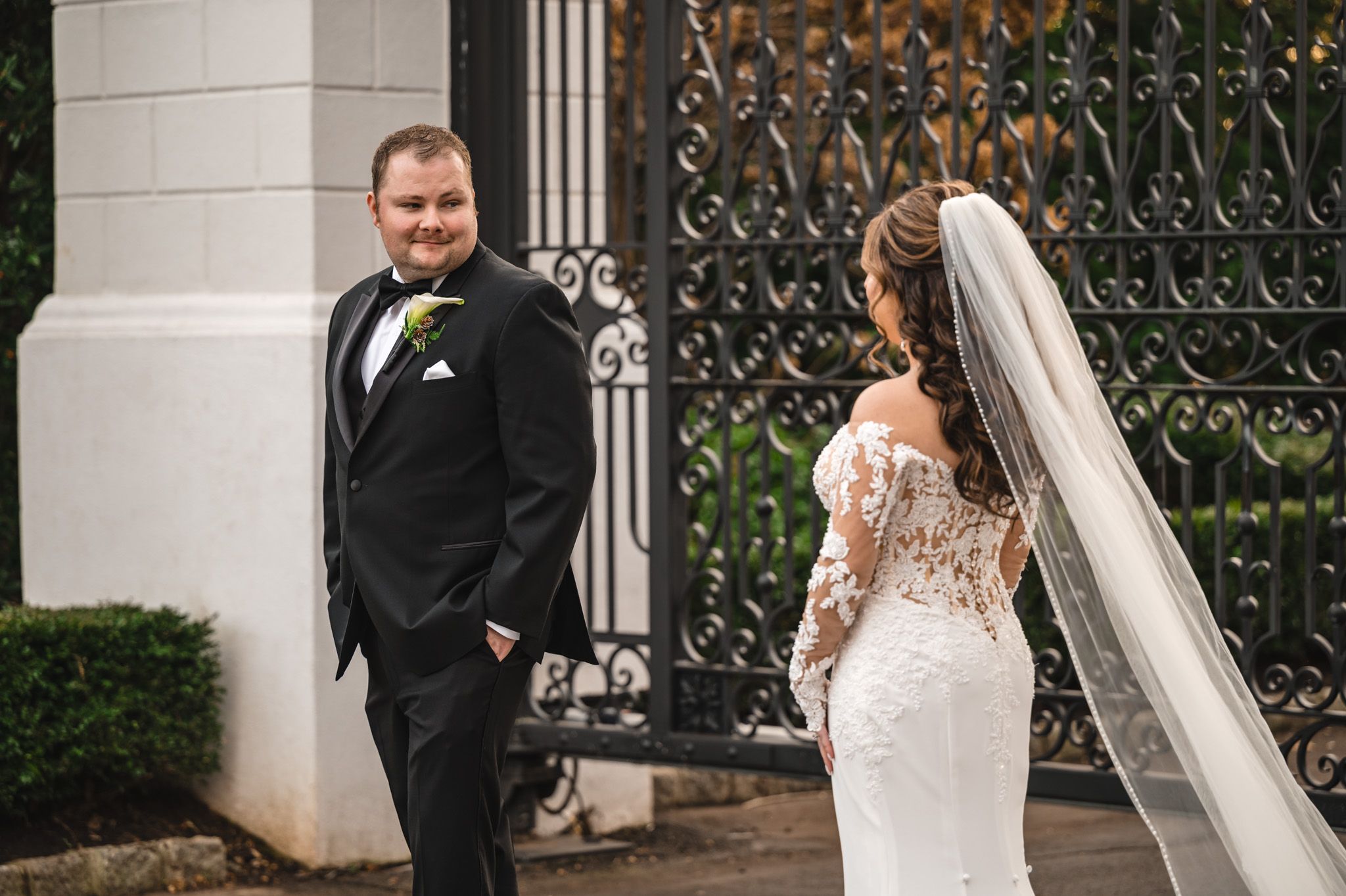 A couple in wedding attire stands by an ornate iron gate during their first look.