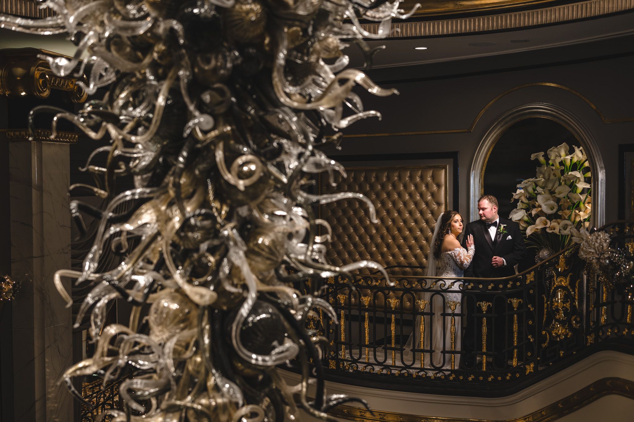 Wedding portraits beneath an elaborate glass chandelier sculpture in an upscale venue.
