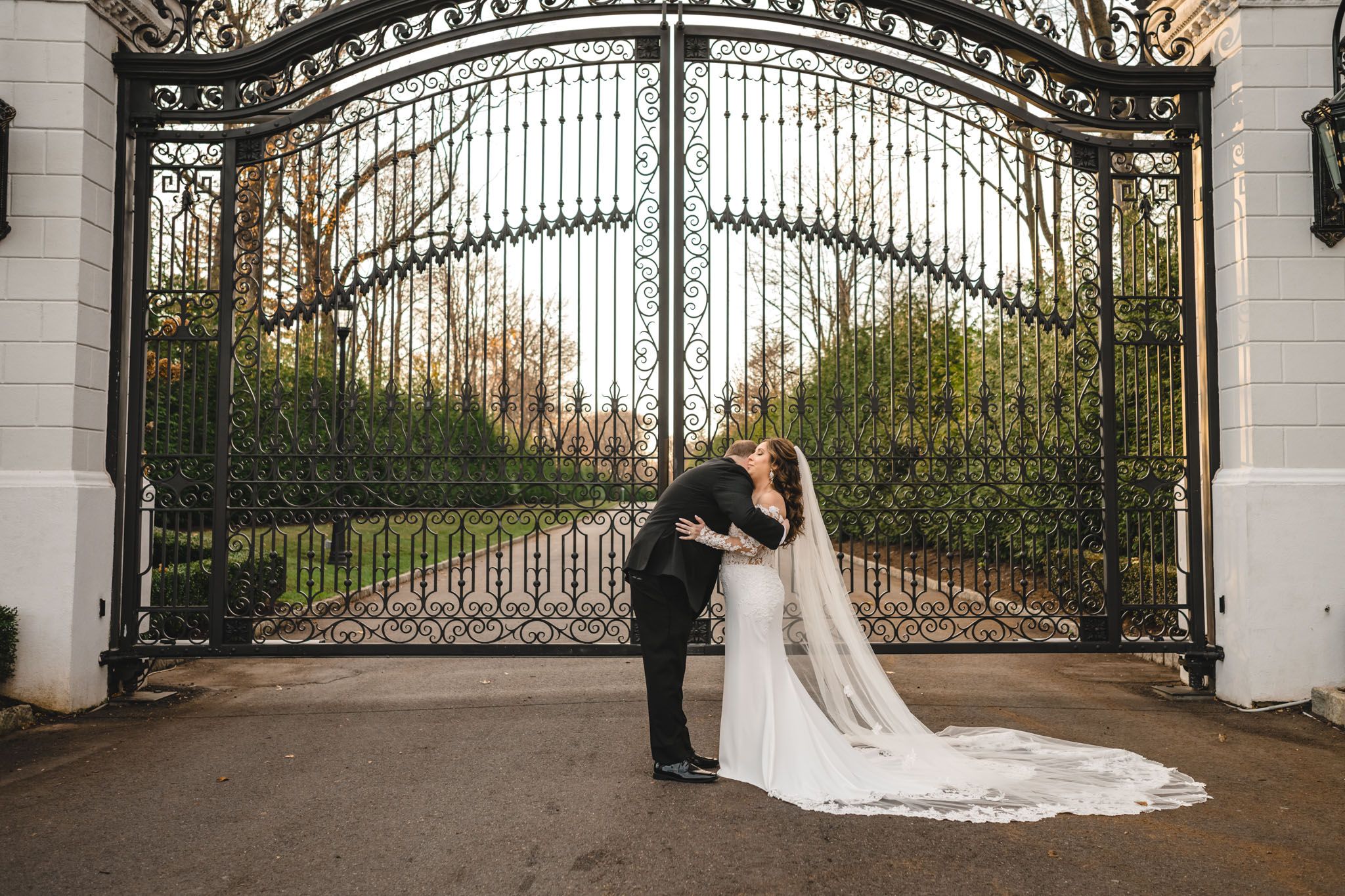 A bride and groom pose dramatically in front of a grand iron gate entrance.