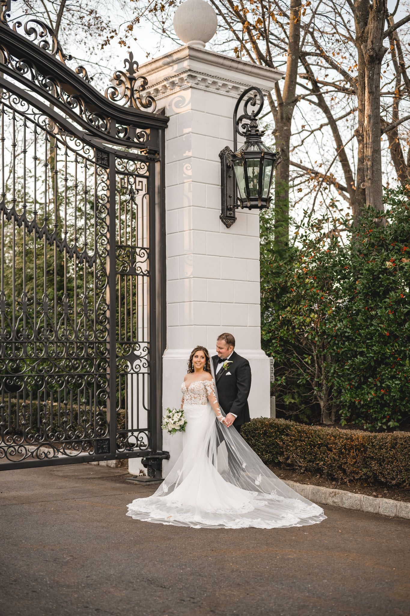 Wedding photos captured near decorative iron gates with white stone pillars and greenery.