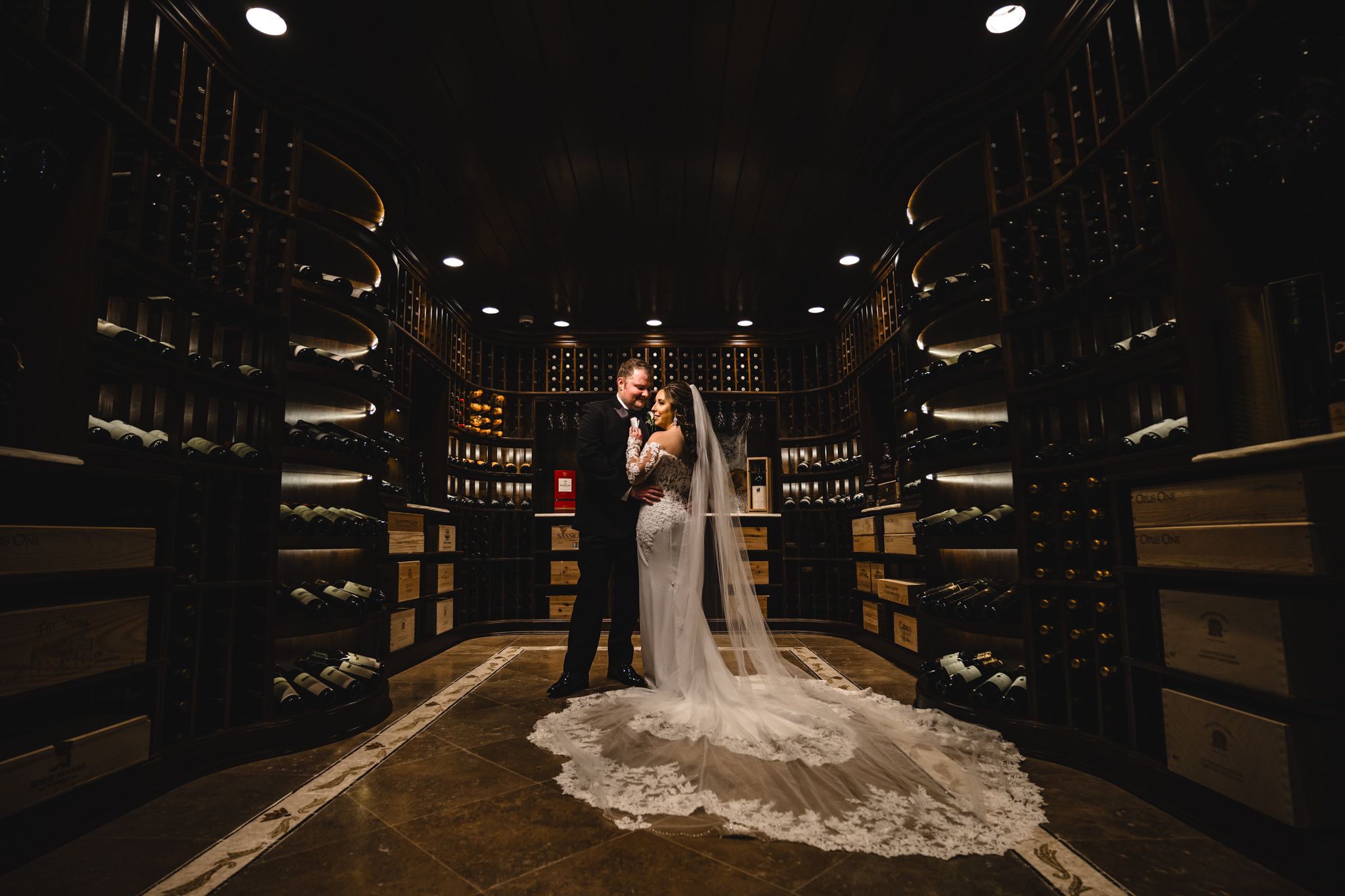 Dramatic wedding photos in a dimly lit wine cellar with wooden barrels and ambient lighting.