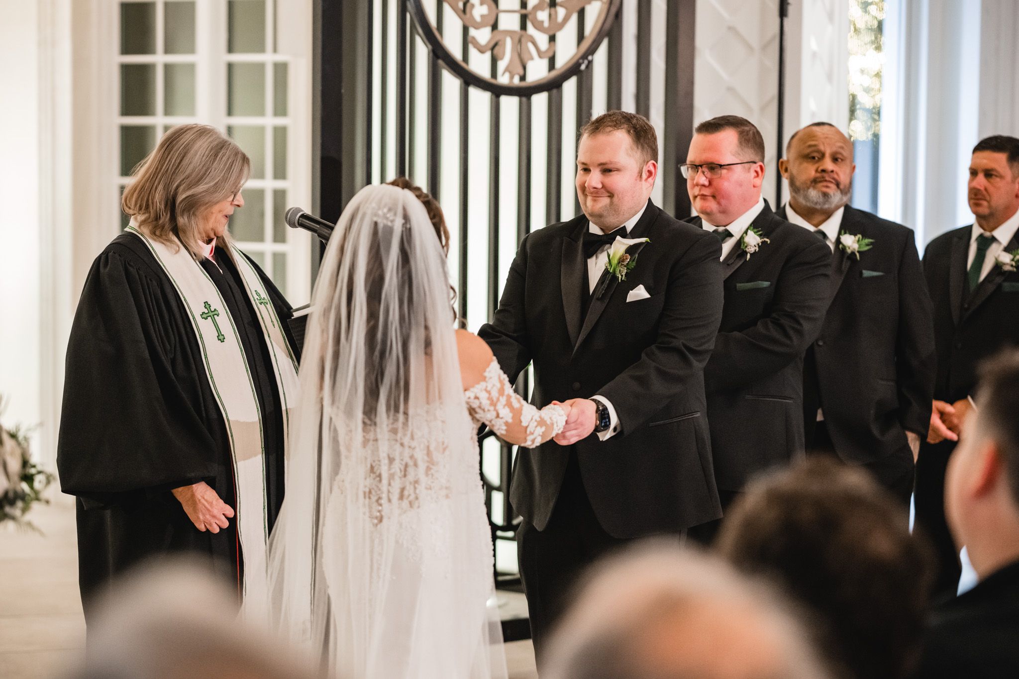 Indoor wedding ceremony with formal attire and decorative lighting in a classic white venue.