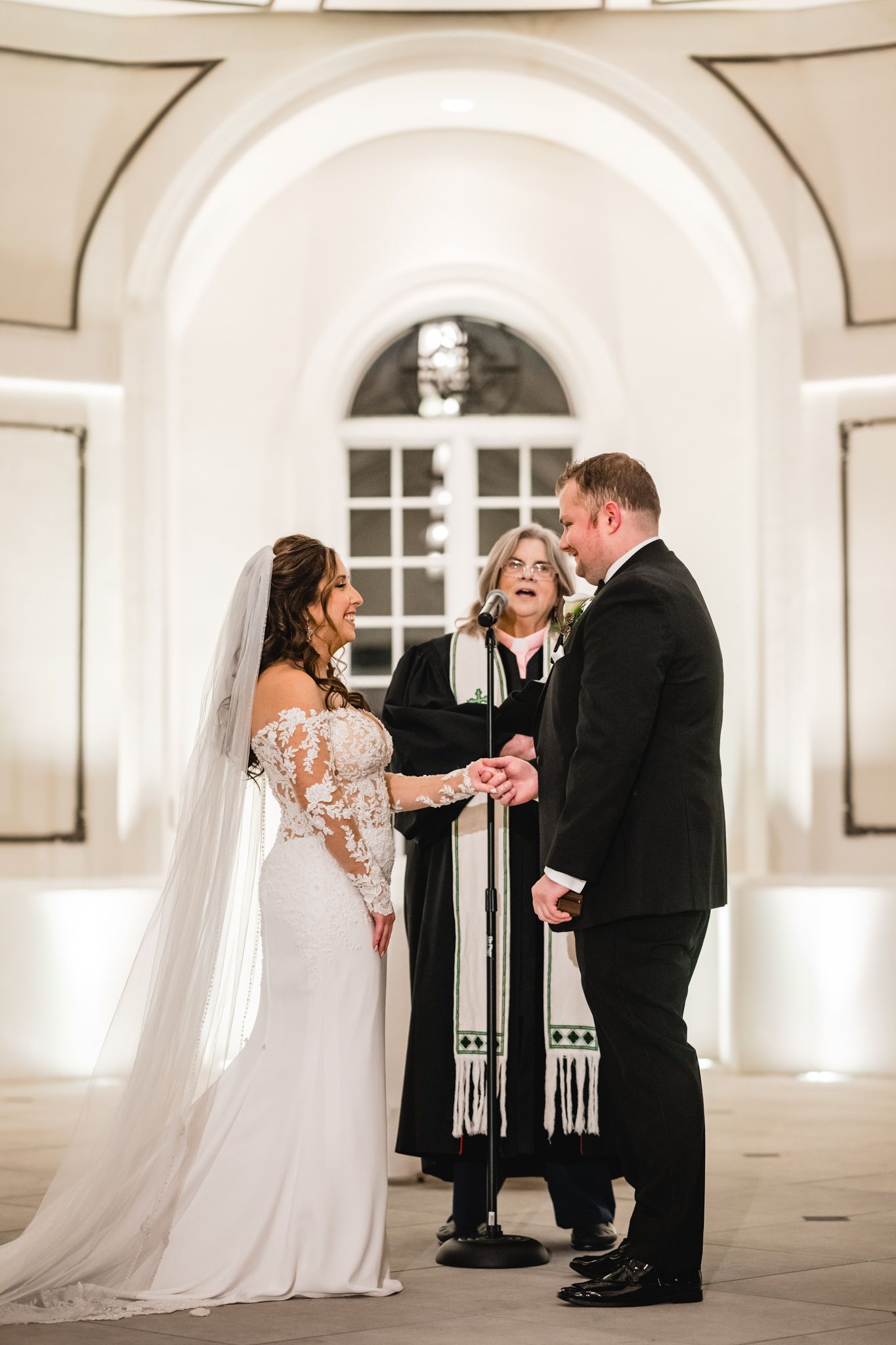 Wedding ceremony proceedings in an elegant white arched room with formal officiant.