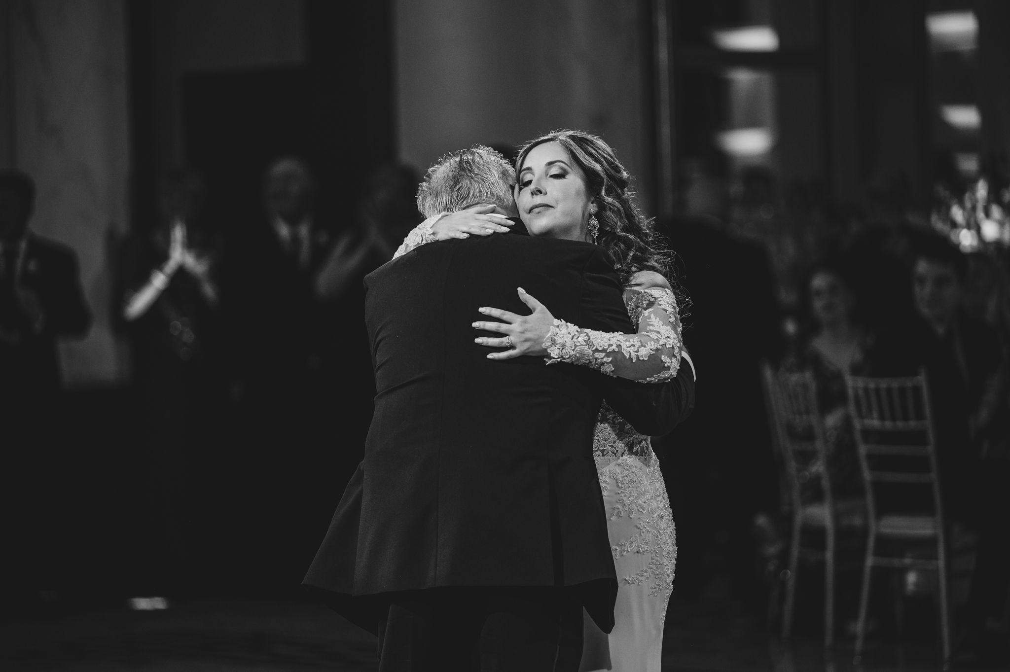 Wedding couple performs an elegant dance move in a dimly lit ballroom with decorative floor patterns.