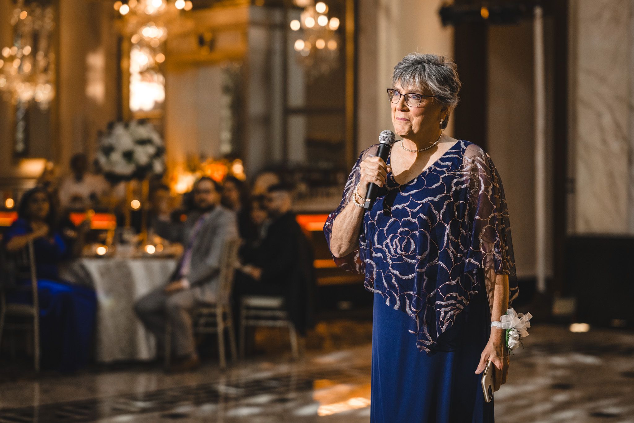 A couple in formal attire poses together in an elegant venue with ornate marble floors and warm lighting.