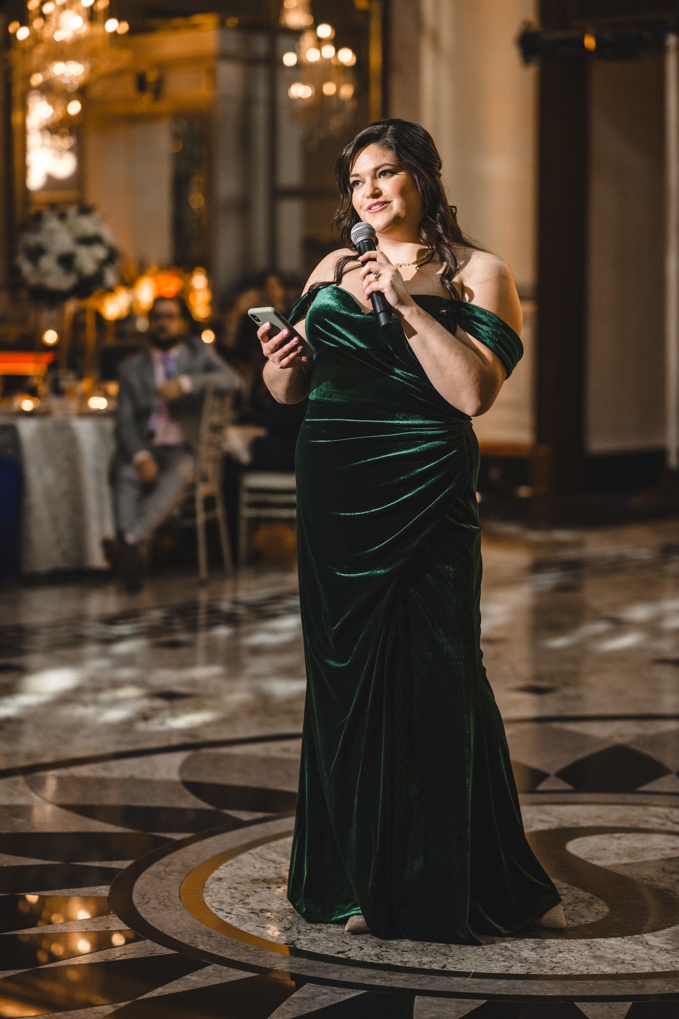 A person in a green velvet dress sits on an ornate marble floor during an elegant photoshoot.