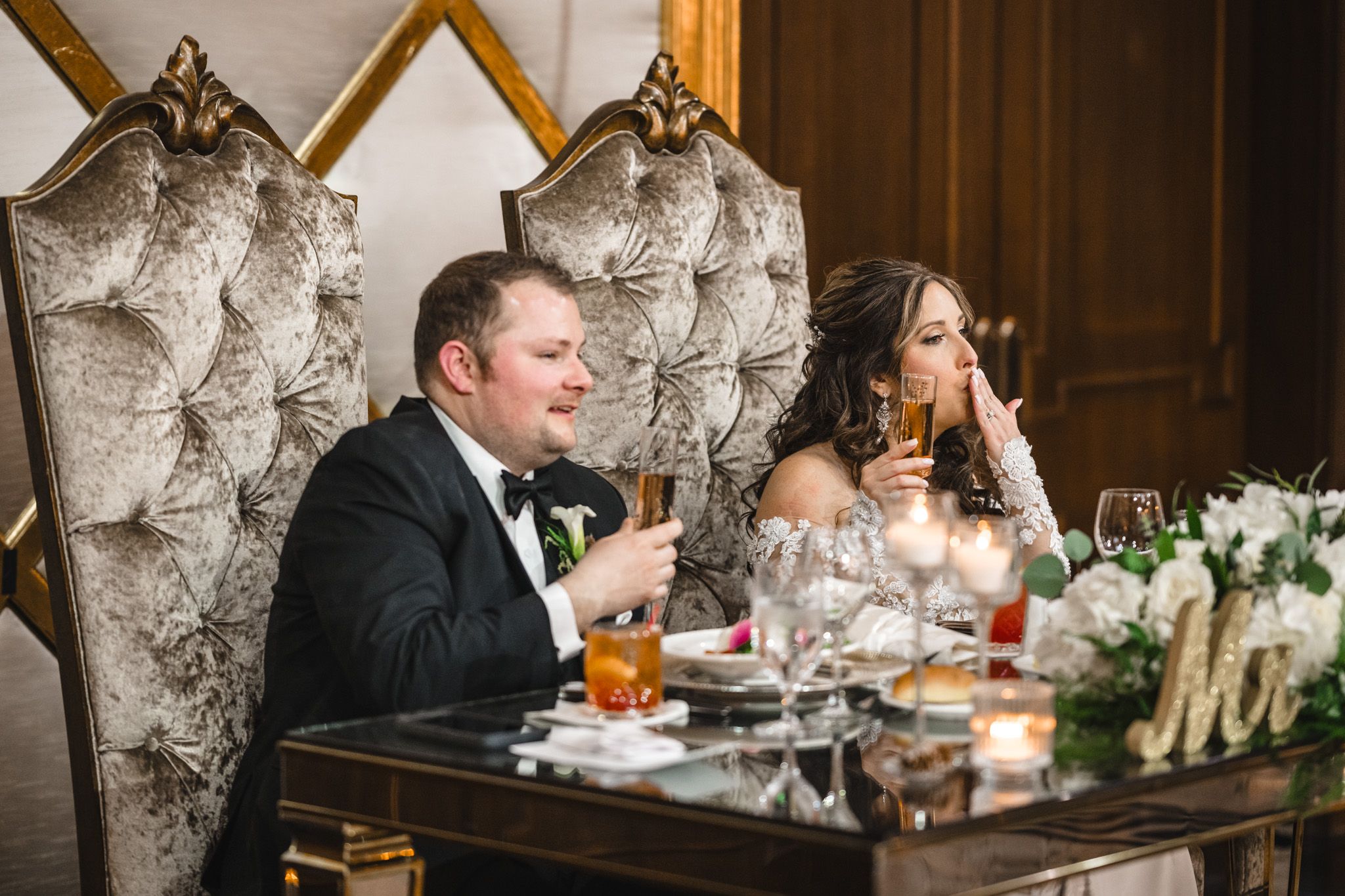 Guests enjoying drinks and conversation at an elegant reception dinner with textured wallpaper backdrop.