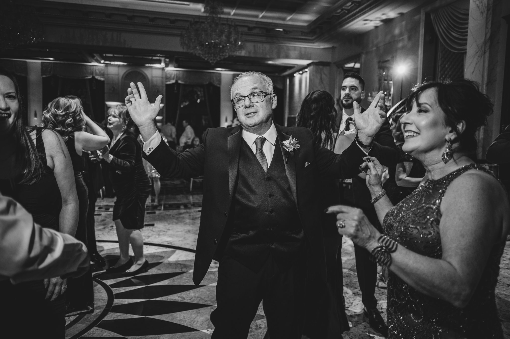 Wedding guests dancing and celebrating in a dimly lit reception venue.