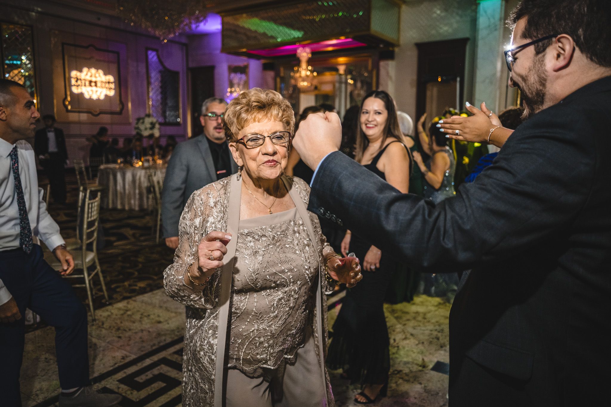 Wedding guests dancing and celebrating with joyful expressions at an evening reception.