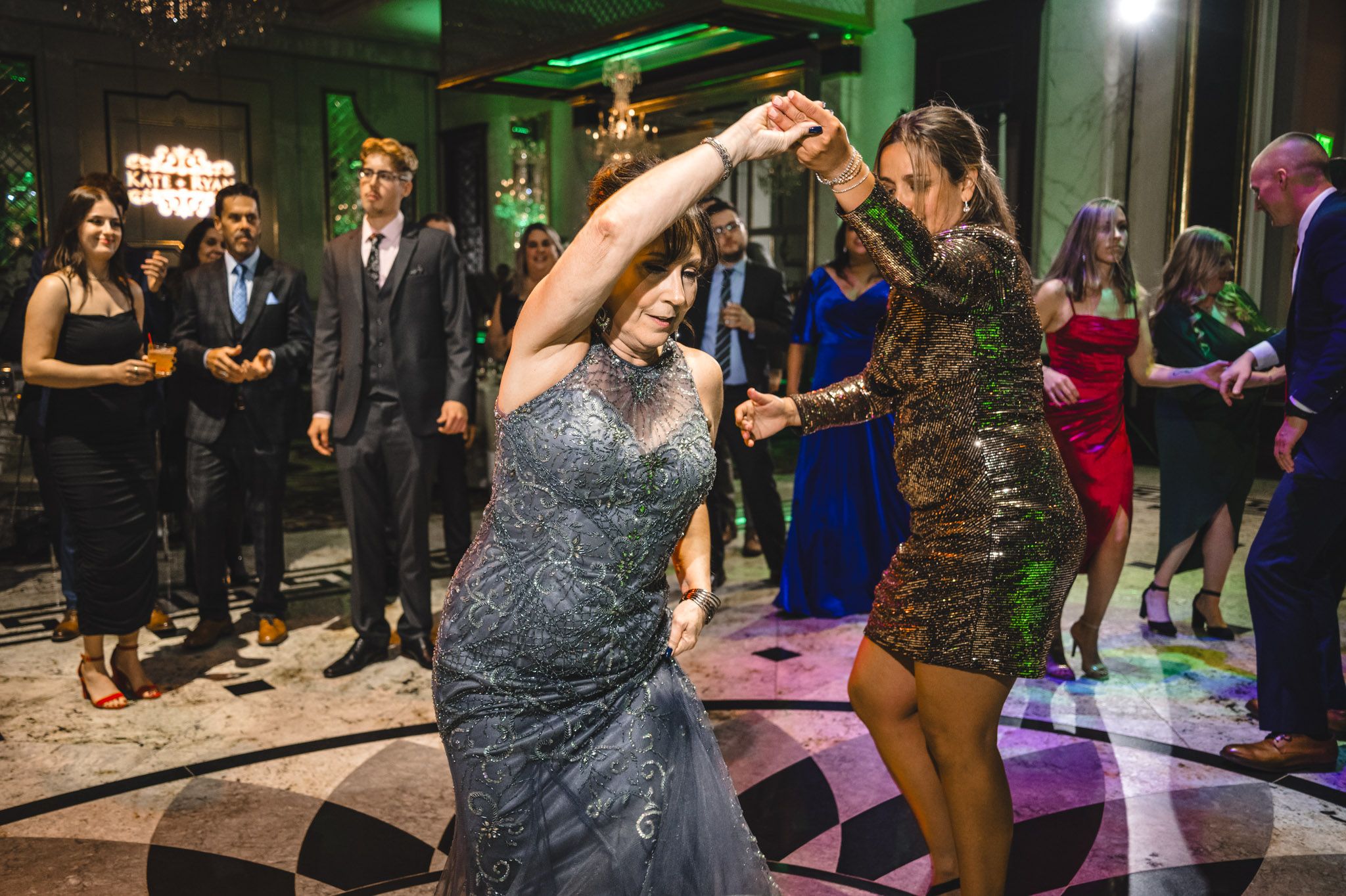 Wedding reception dance floor filled with guests under green and purple mood lighting.