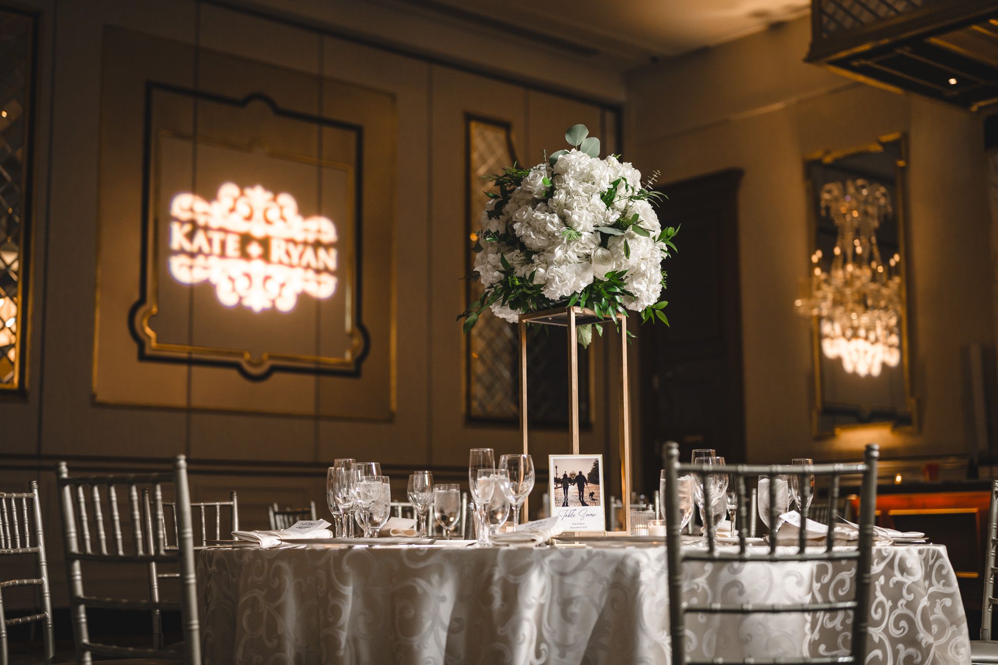 Elegant wedding reception venue with crystal chandeliers and white floral centerpieces on round tables.