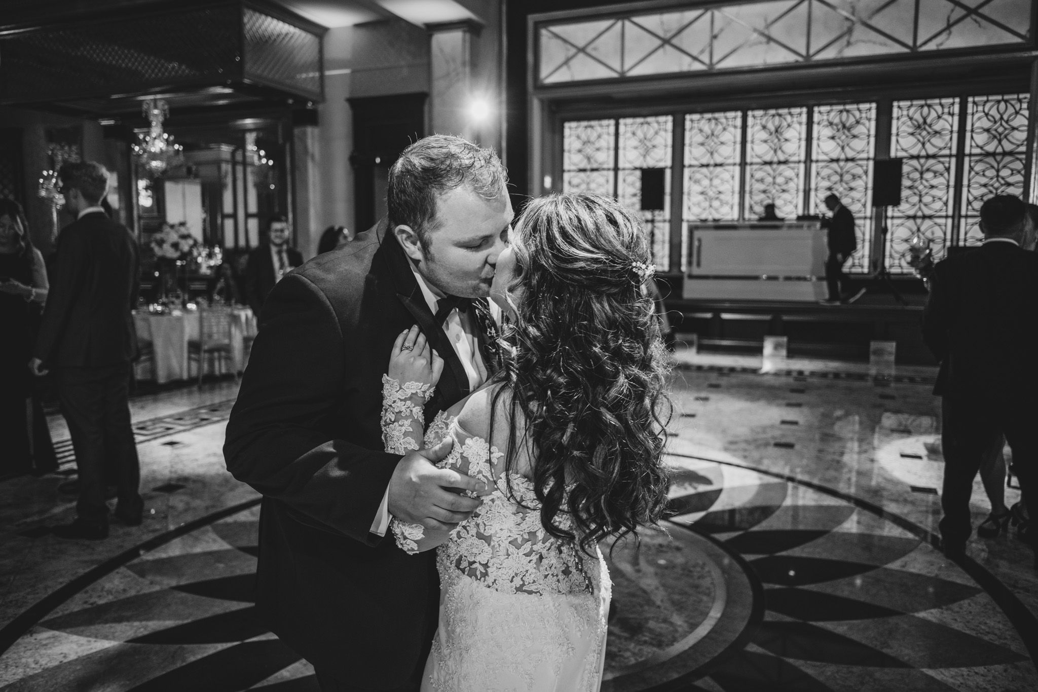 Wedding reception venue with elegant ceiling details and guests dancing in formal attire.