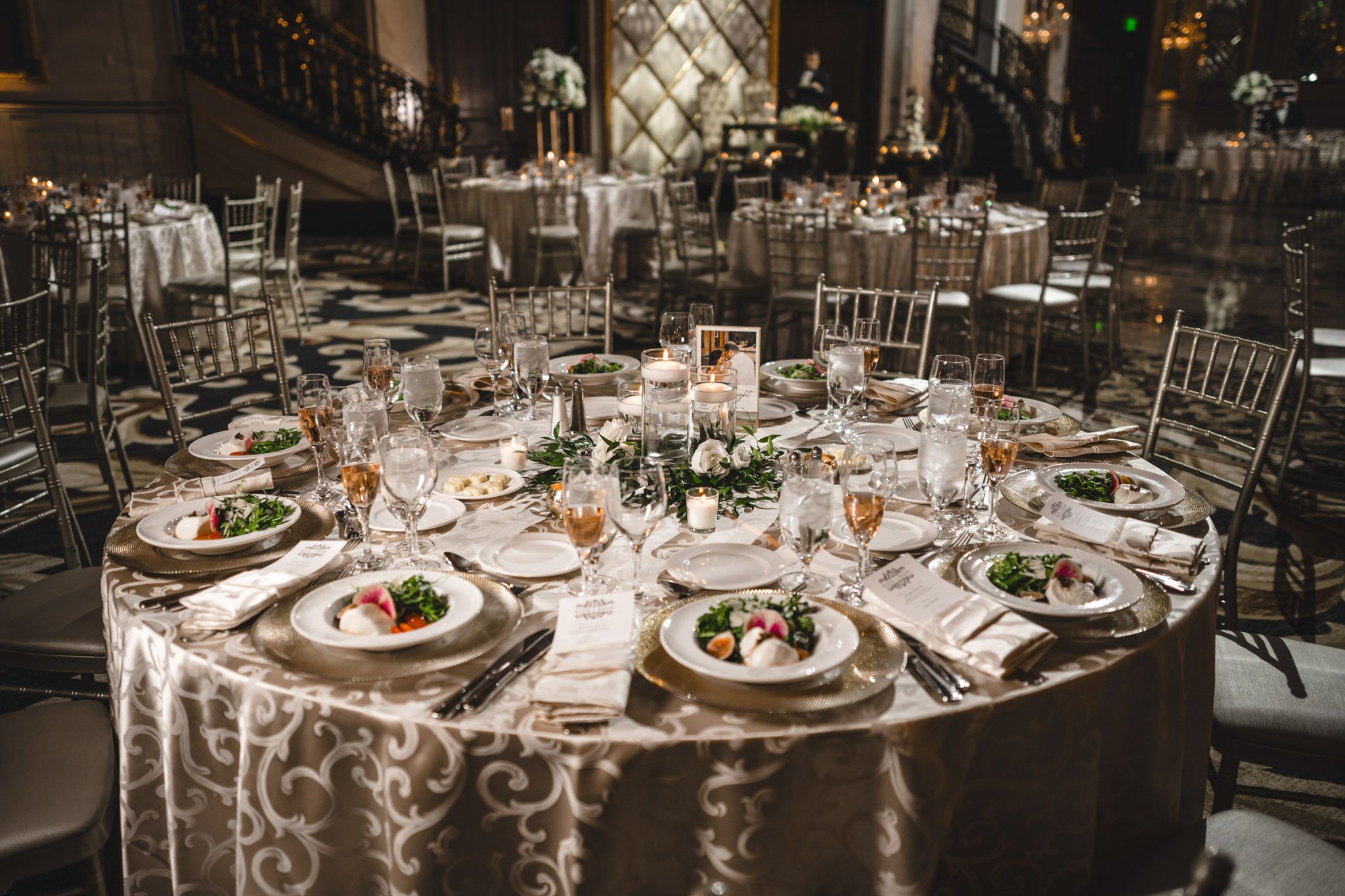 Round reception tables set with elegant place settings and floral centerpieces in a dimly lit ballroom.
