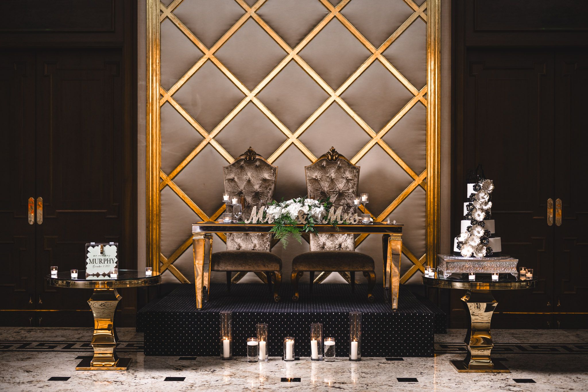 Gold geometric wall panels with uplighting create an elegant backdrop for wedding reception decor.