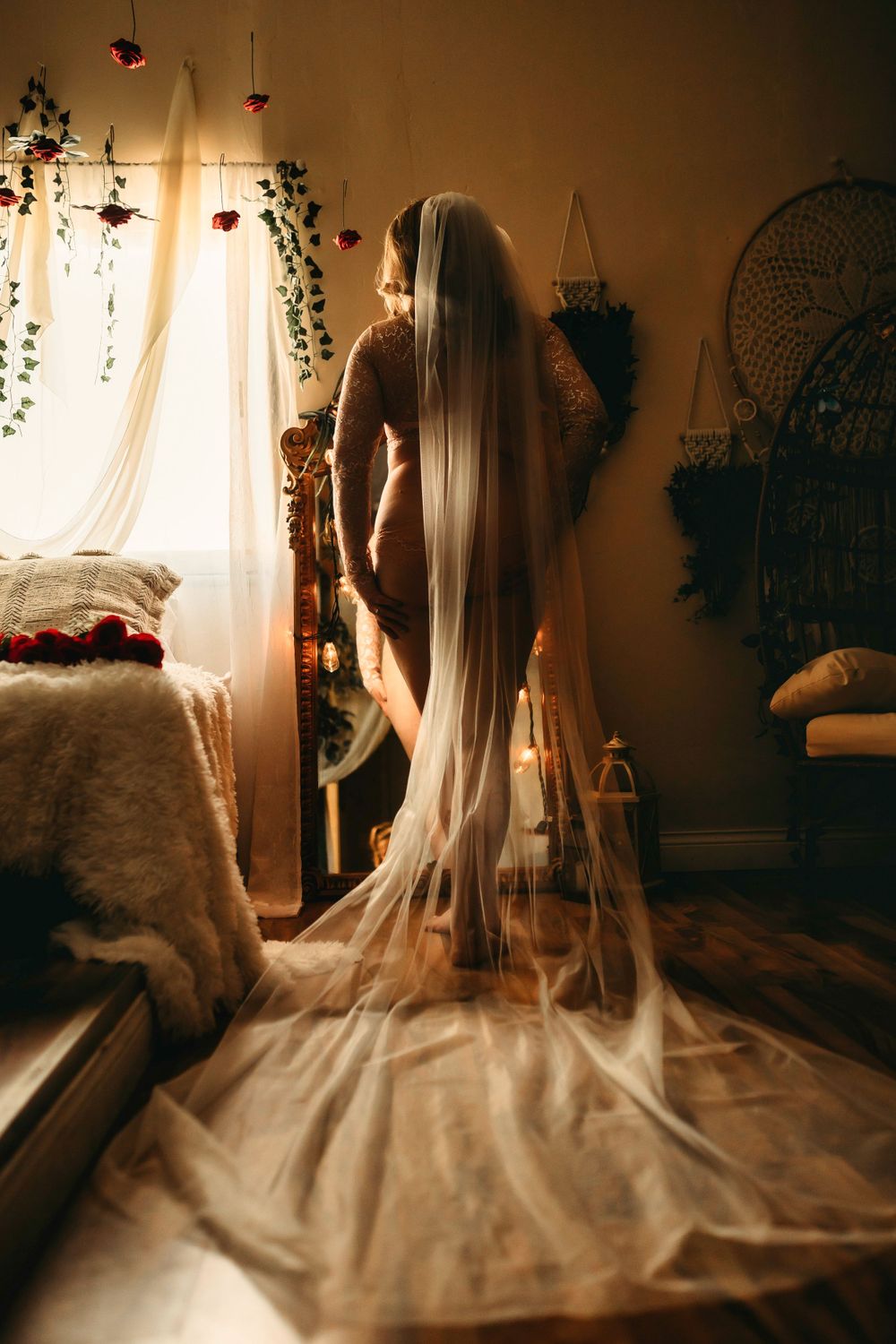 A long flowing white bridal veil cascades down in a romantic boudoir setting with soft lighting and hanging plants.