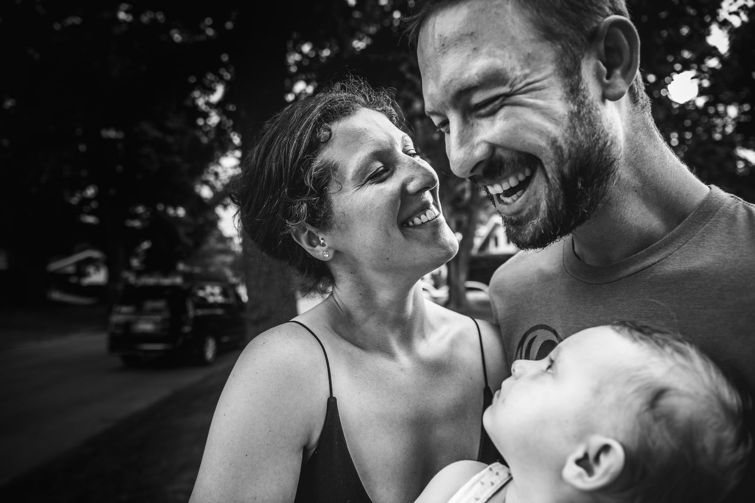 A woman and man smile broadly as they hold their young daughter who is looking up at them.
