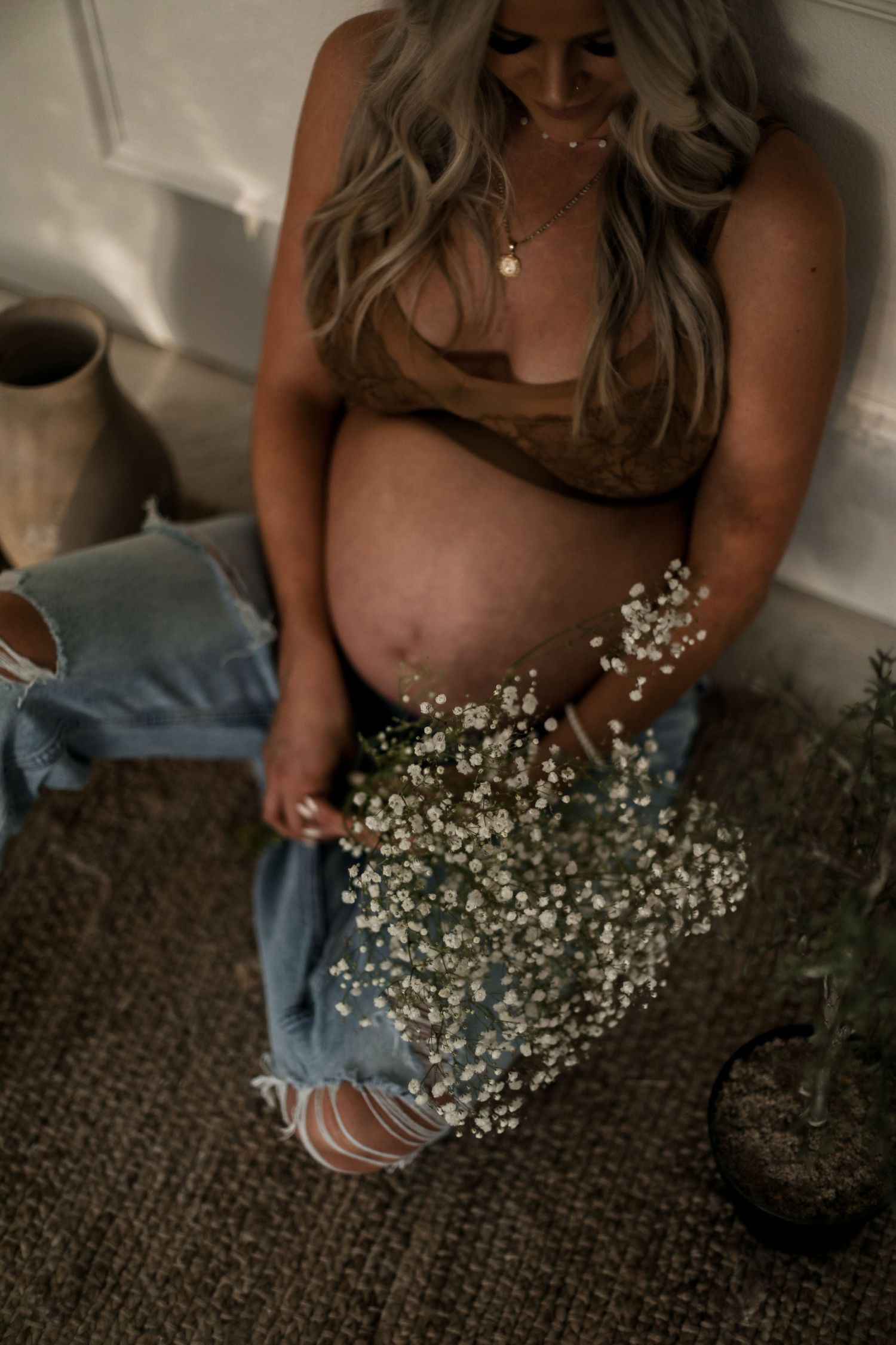 Baby's breath flowers held over a maternity scene with distressed denim and brown top.