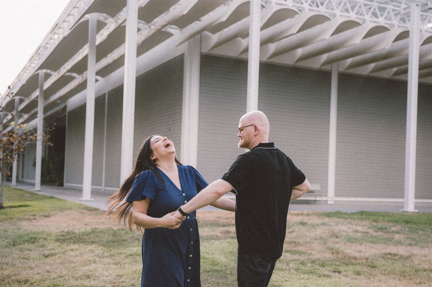 A couple shares a joyful moment in front of a white columned building.