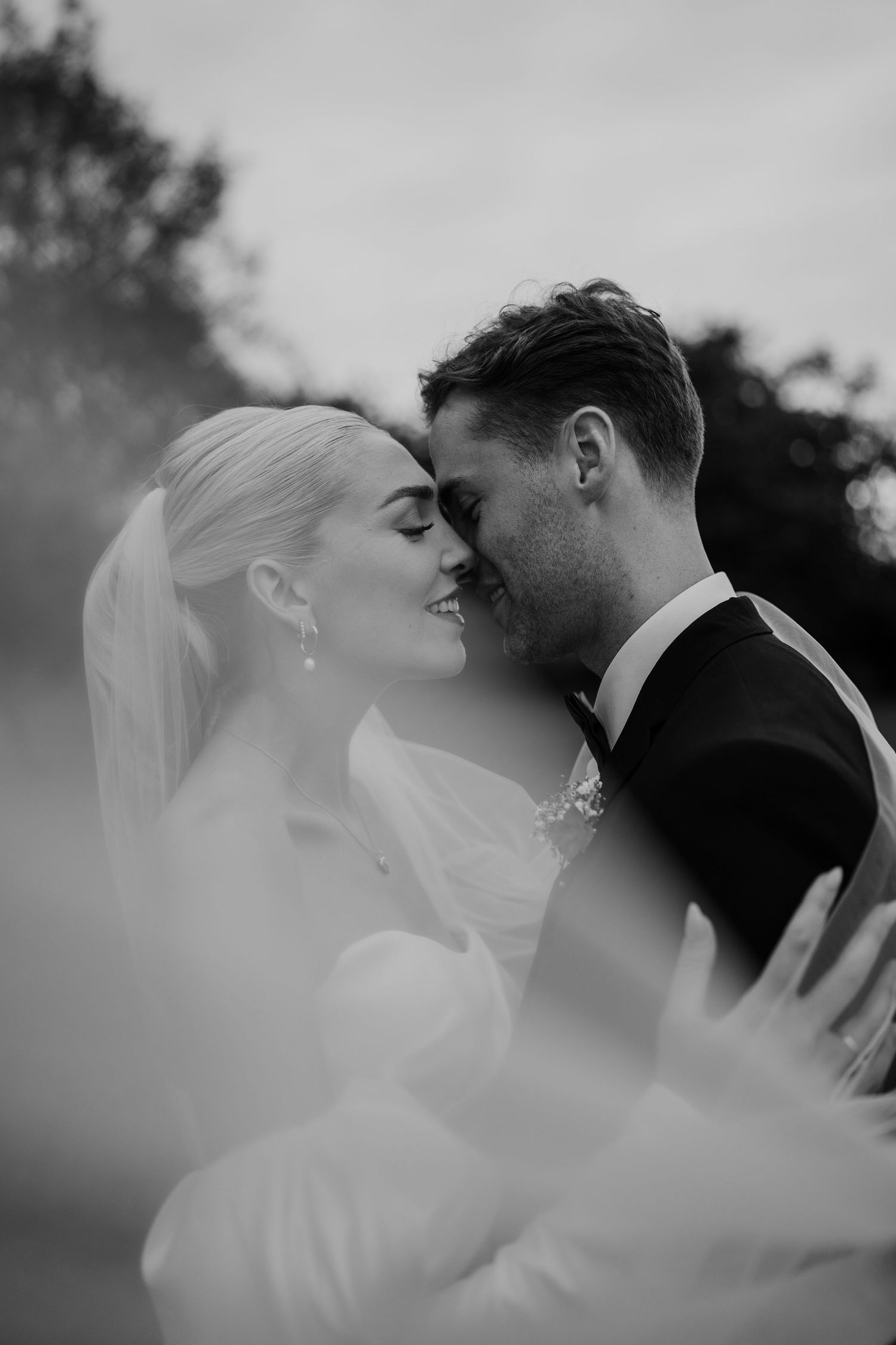 Bride and groom kissing. Bride wearing pearl jewellery and groom is wearing black tie tux.