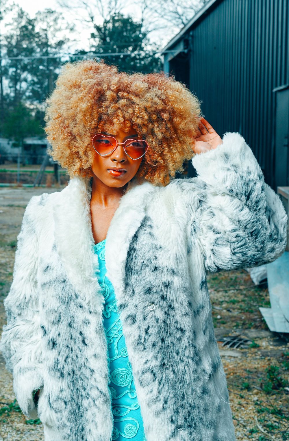 Fashionable model in fluffy white fur coat and orange sunglasses poses outdoors.