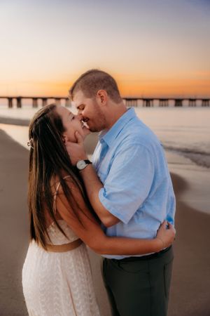 Romantic beach engagement photo at sunset with pier in background.