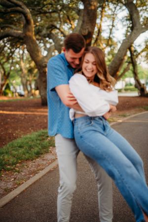 Couple sharing playful dance move on path with trees and golden light.