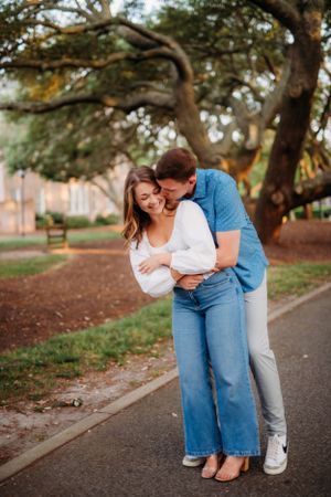 Couple embracing and laughing together on park pathway with autumn trees in background.