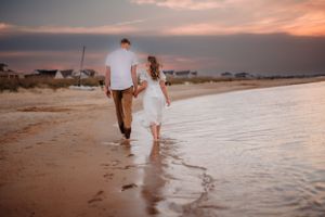 Couple walks hand in hand along beach shoreline during golden sunset.