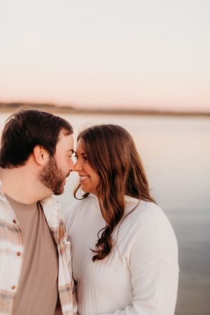 A romantic coastal portrait session featuring a couple in matching white sweaters at sunset.