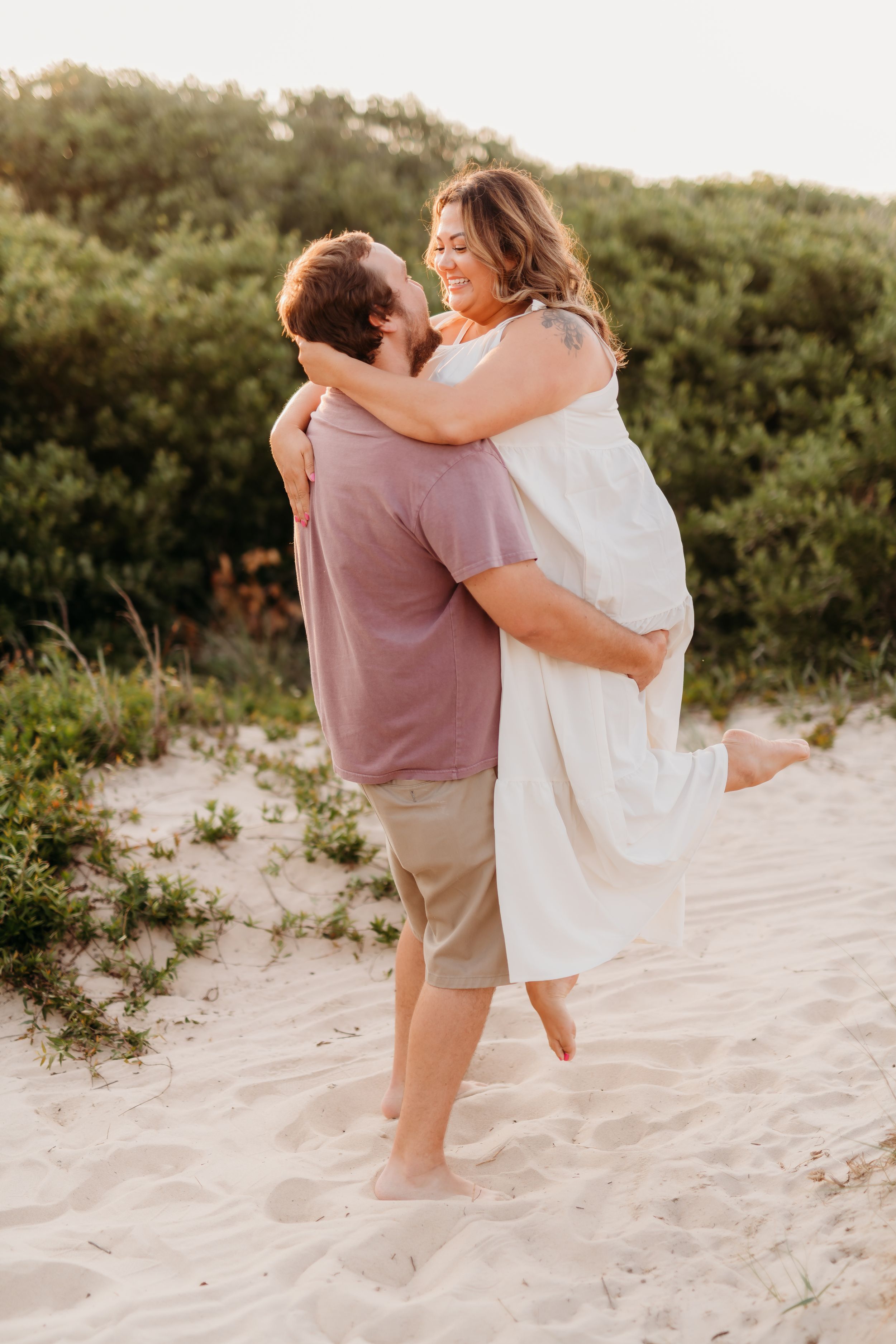 Playful couple sharing a joyful moment on sandy beach dunes.